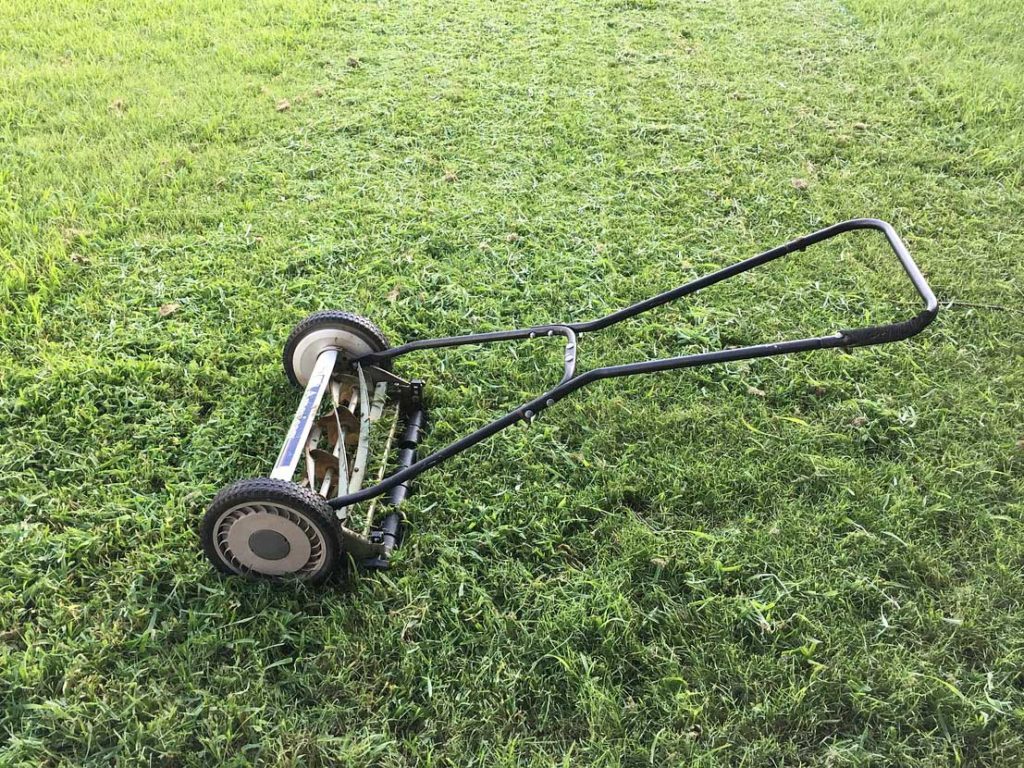 A human-powered lawn mower is shown on a green lawn in Spoken Garden's "Top Fall Garden Tasks" post. 