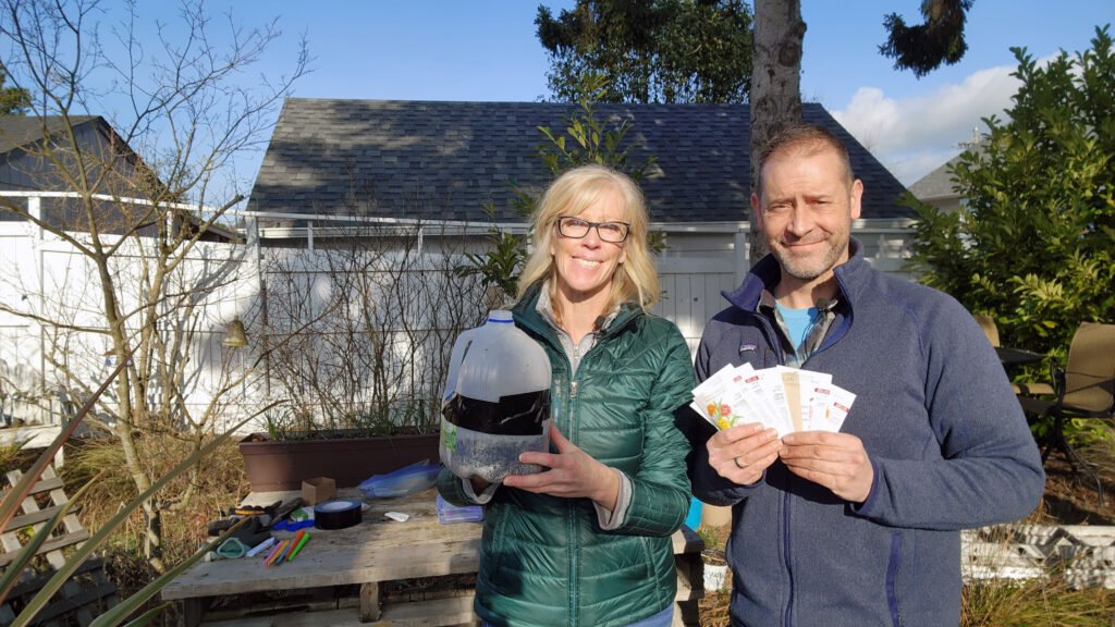 Sean and Allison McManus in their garden holding seed packets and seed jug planter.